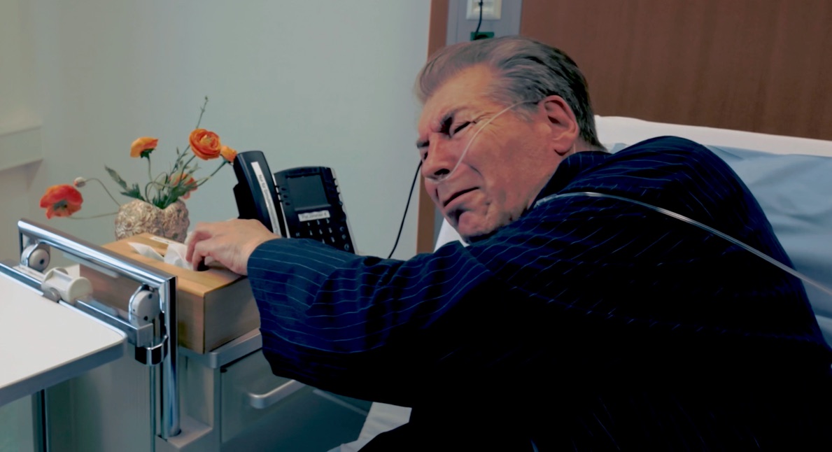 Standbild aus dem Video zum Fall: ein Patient im Krankenhausbett greift nach seinem Nachttisch